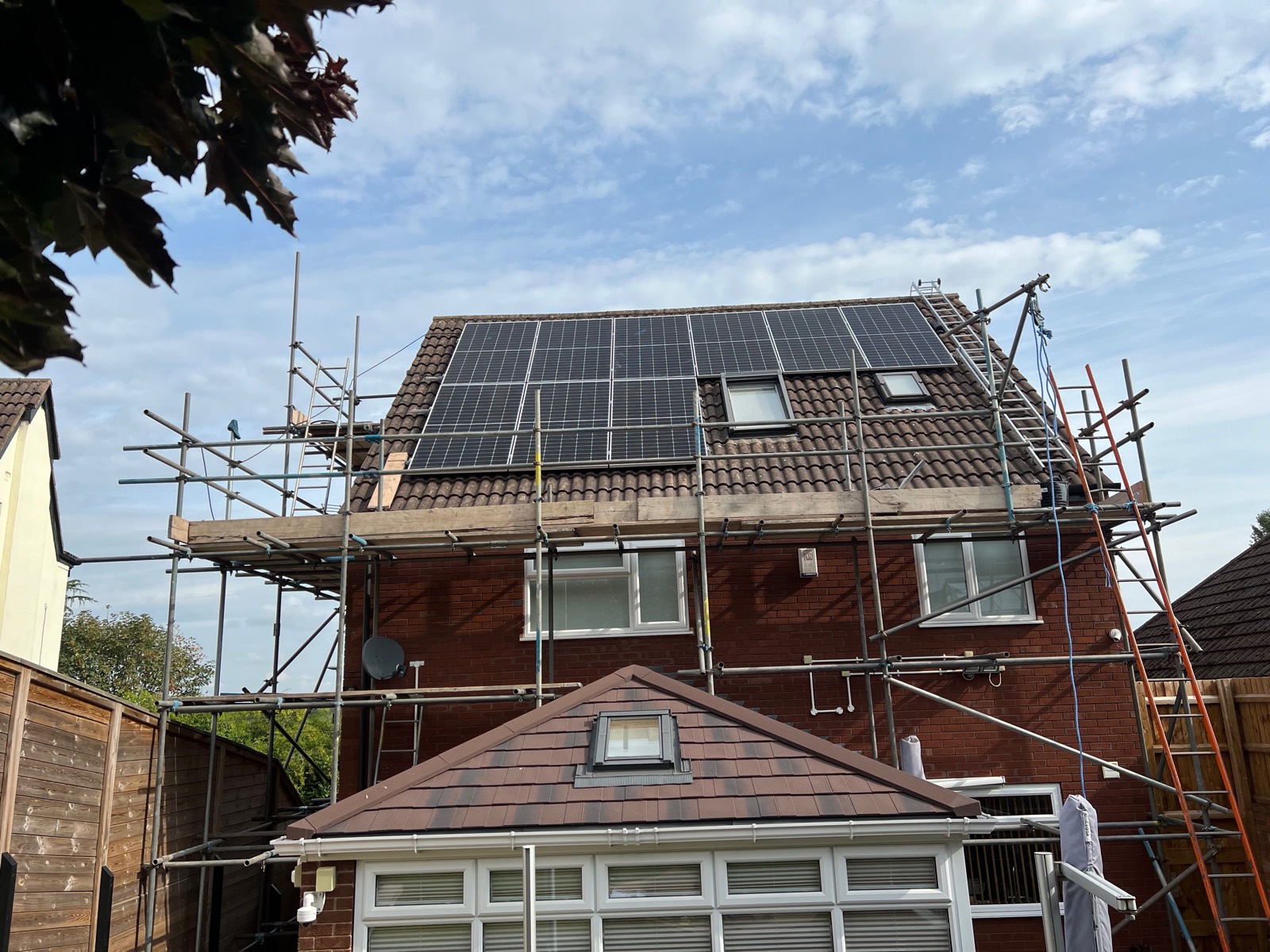 Scaffold up, mid-install: panels clamped onto rails above the tiles.